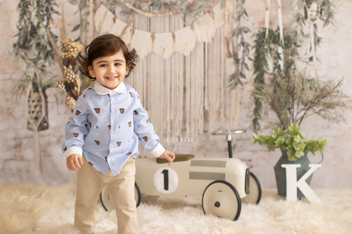 Delhi and Gurgaon offer the perfect backdrop for your little boy's milestone photoshoot with Anega Bawa Photography. Seated on a white rug with a toy scooter nearby, against a backdrop of lush leafy pots and a clean white backdrop, your 12-month to 1-year-old is captured in moments of pure joy and innocence, creating cherished memories to last a lifetime.