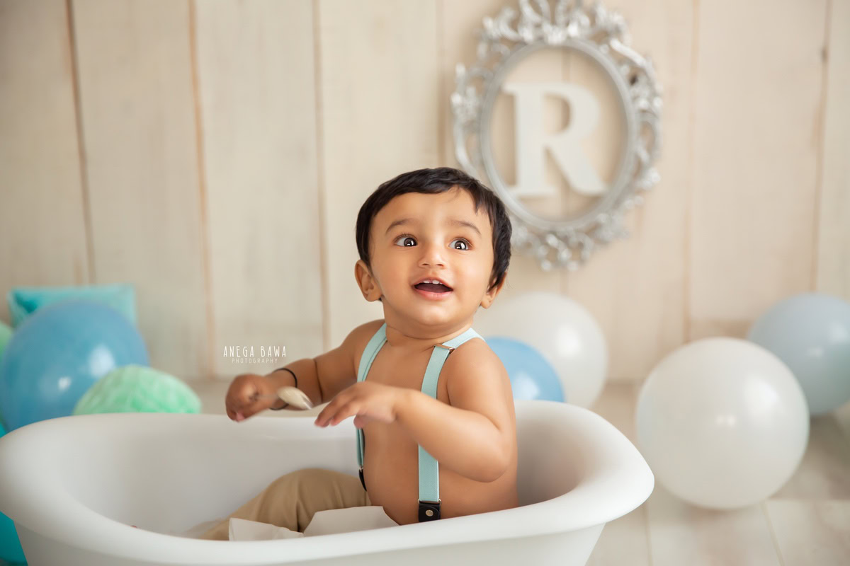 Delhi and Gurgaon set the stage for delightful moments in your little boy's photoshoot by Anega Bawa Photography. Picture him seated in a white tub surrounded by colorful balloons, against a warm beige backdrop, capturing the essence of his innocence and playfulness at 12 months to 1 year old.