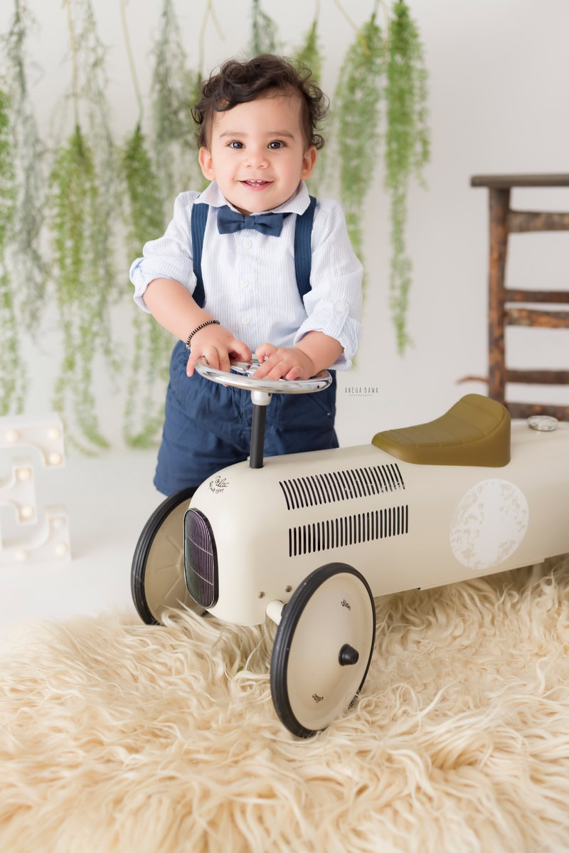 Delight in the playful innocence of your little one with Anega Bawa's sitter photography in Delhi & Gurgaon. Capturing the joy of childhood, this session features your 12-month to 1-year-old boy with his favorite toy scooter, seated on a beige rug adorned with a leafy fringe. Against a pristine white backdrop, each moment is beautifully preserved for you to treasure forever.