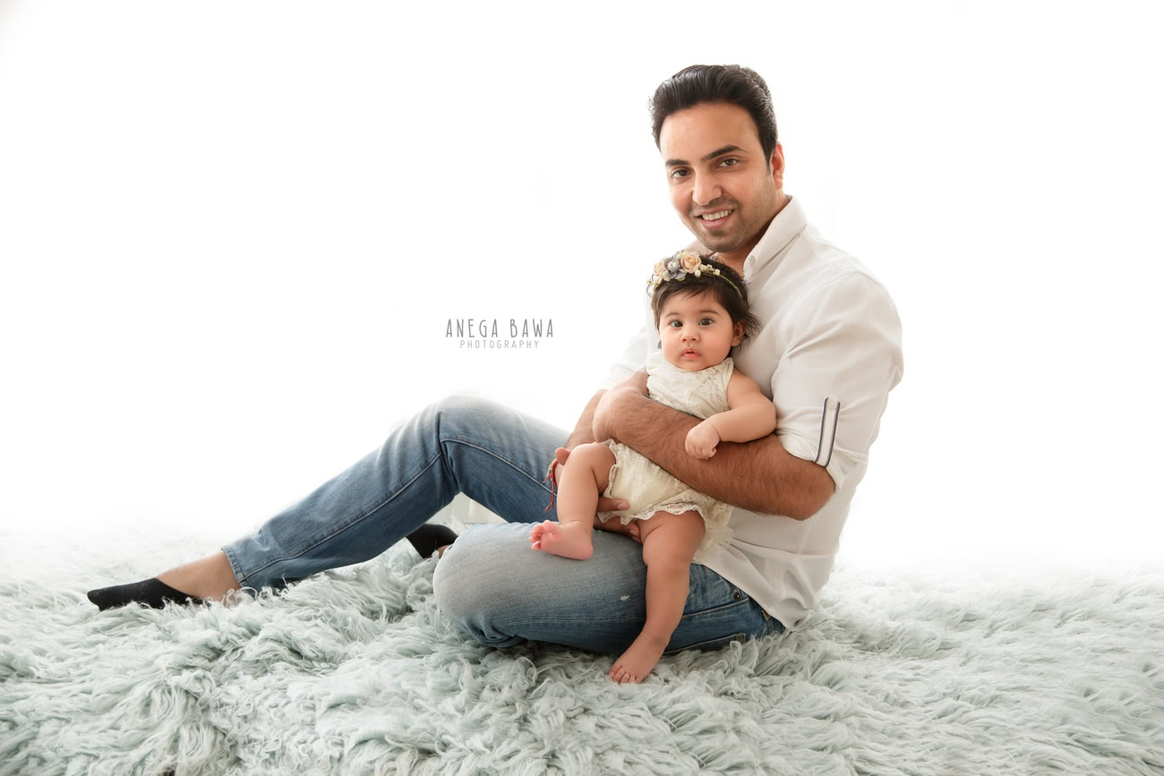 Capture the bond between Dad and daughter with Anega Bawa Photography in Delhi and Gurgaon. In this heartwarming family photoshoot, Dad holds his little one on a cozy grey rug against a clean white backdrop, creating timeless memories to cherish forever.
