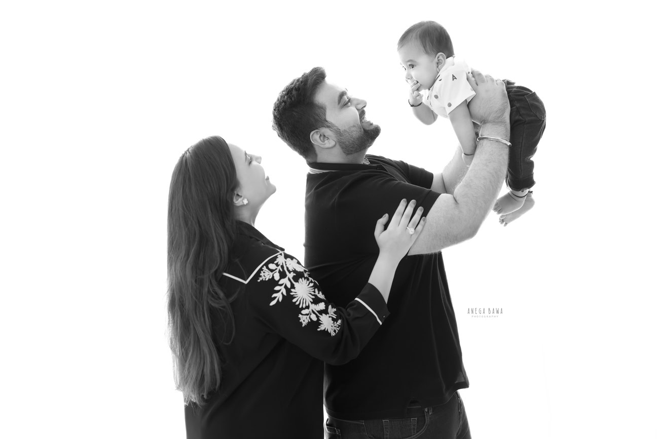 Create lasting memories with Anega Bawa Photography in Delhi and Gurgaon as Dad engages in playful moments with his son while Mom strikes a pose against a serene white backdrop. Capture the essence of family love and joy in every frame with our expert photography services.