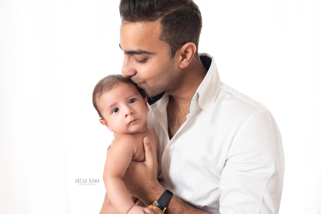 In Delhi and Gurgaon, against a serene white backdrop, Anega Bawa Photography captures the tender moment of father and son sharing a loving kiss, immortalizing the bond between them in a timeless photograph filled with warmth and affection.