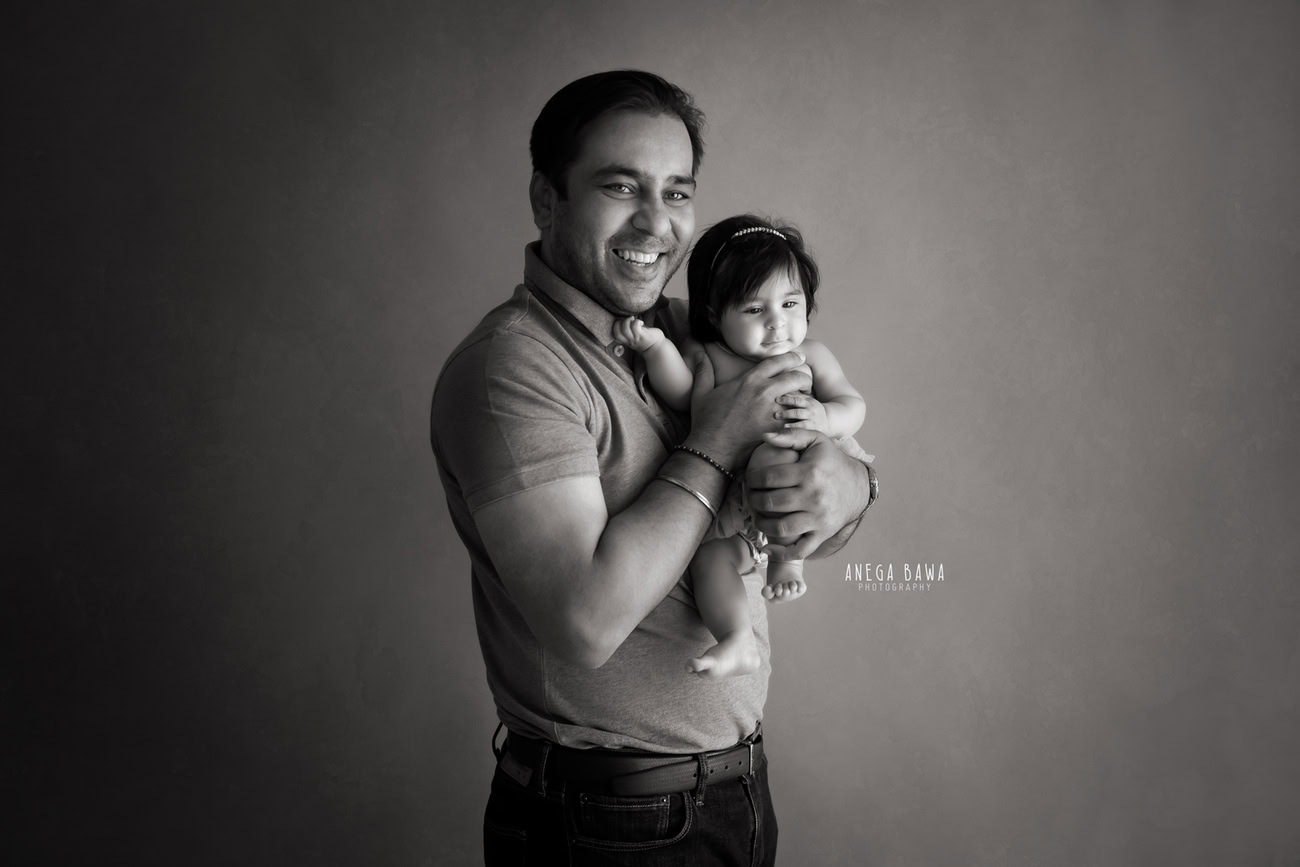 Create timeless memories with Anega Bawa Photography in Delhi and Gurgaon as a proud dad cradles his daughter in a classic black-and-white pose against an elegant backdrop. Let the love and connection between father and daughter be immortalized in every frame, capturing the essence of this beautiful bond.