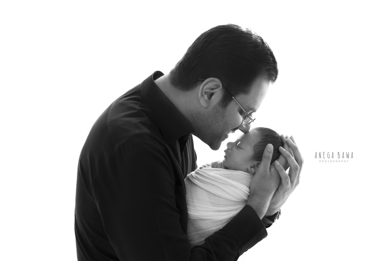 Capture heartwarming moments with Anega Bawa Photography in Delhi and Gurgaon as a loving dad shares a tender kiss with his son, wrapped in white, against a pristine backdrop. Let the purity of this bond shine through in every frame, preserving the warmth and affection for years to come.