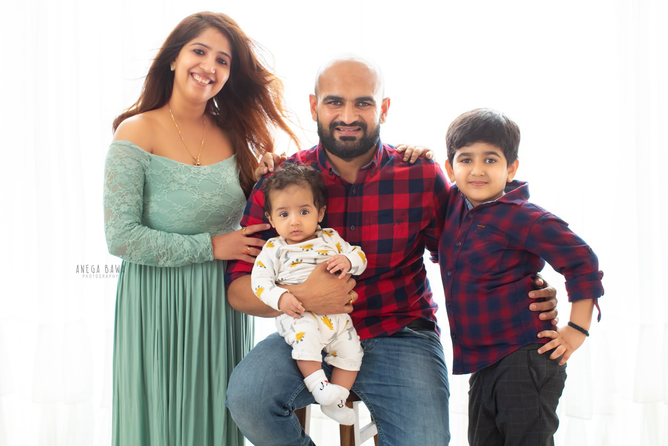 Charming family photoshoot by Anega Bawa Photography, the esteemed photographer in Delhi and Gurgaon, showcasing the loving bond between Mom, Dad, and their precious 3, 4, 5, 6-month-old daughter, with sibling, against a serene white backdrop.