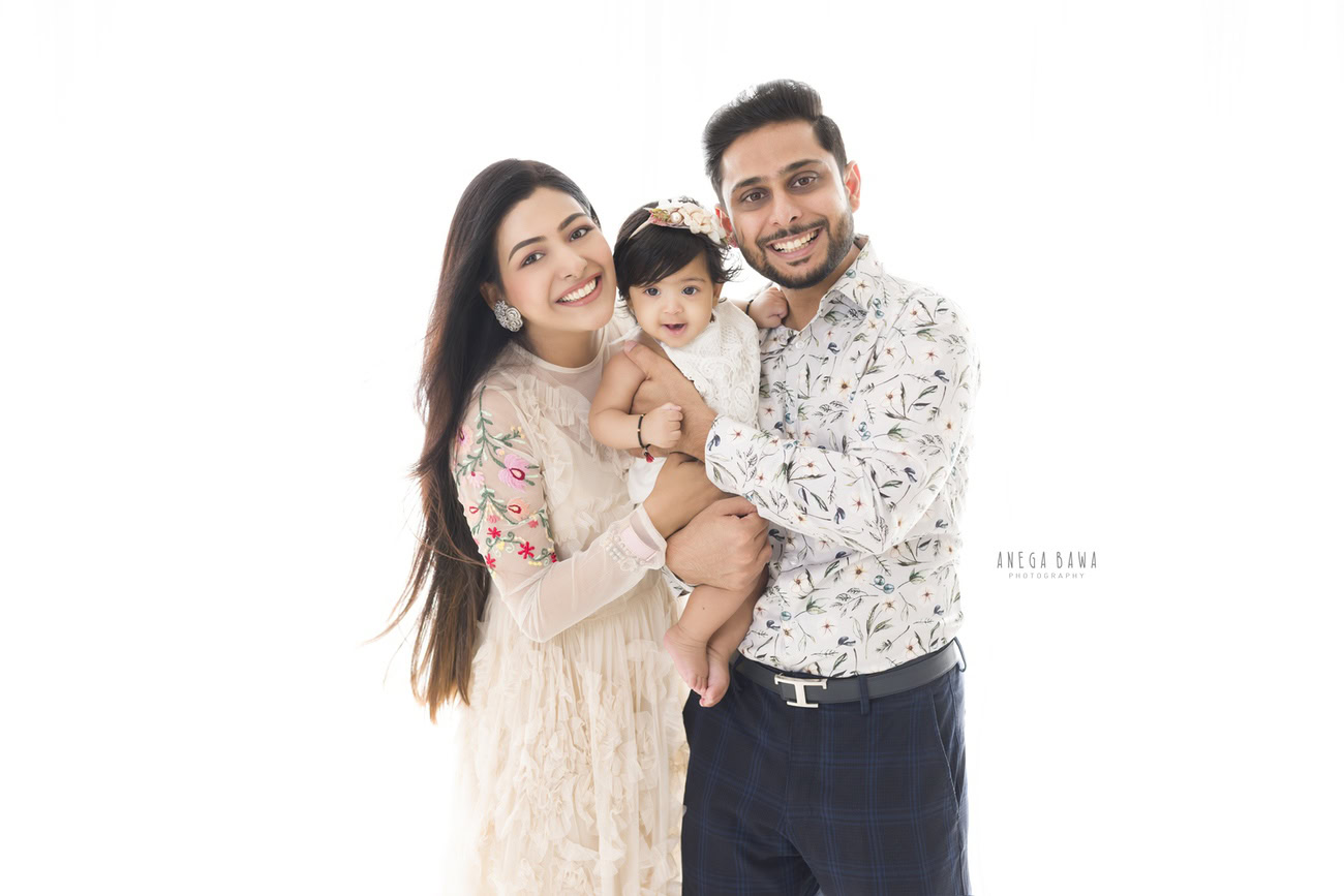 Captivating family photoshoot by Anega Bawa Photography, the esteemed photographer in Delhi and Gurgaon, capturing the tender moments of Mom and Dad holding their precious 3, 4, 5, 6-month-old daughter against a pristine white backdrop.