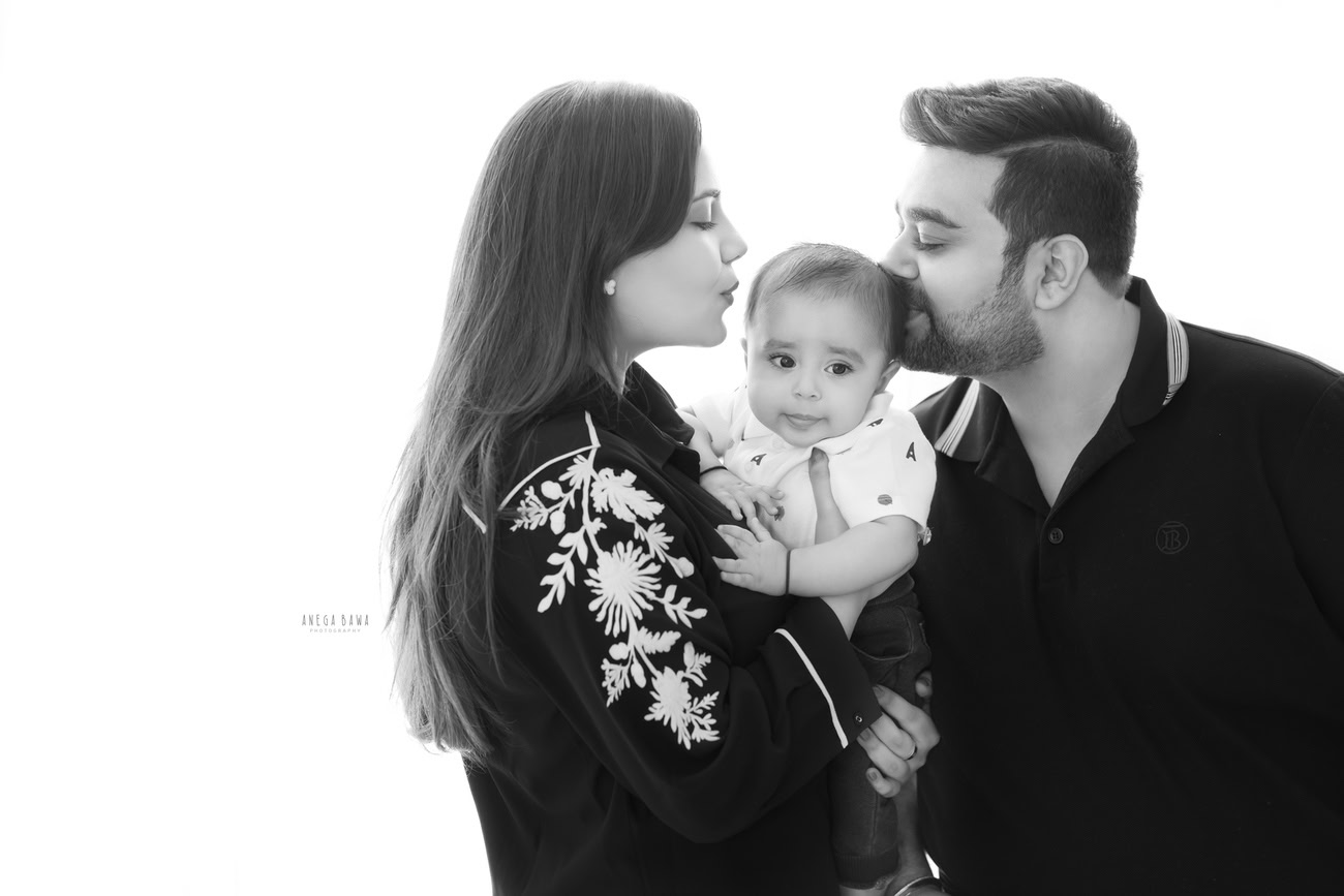 Cherished family photoshoot by Anega Bawa Photography, the esteemed photographer in Delhi and Gurgaon, capturing the heartwarming moments of Mom, Dad, and their adorable 3, 4, 5, 6-month-old son in a cute kissing pose against a serene white backdrop.