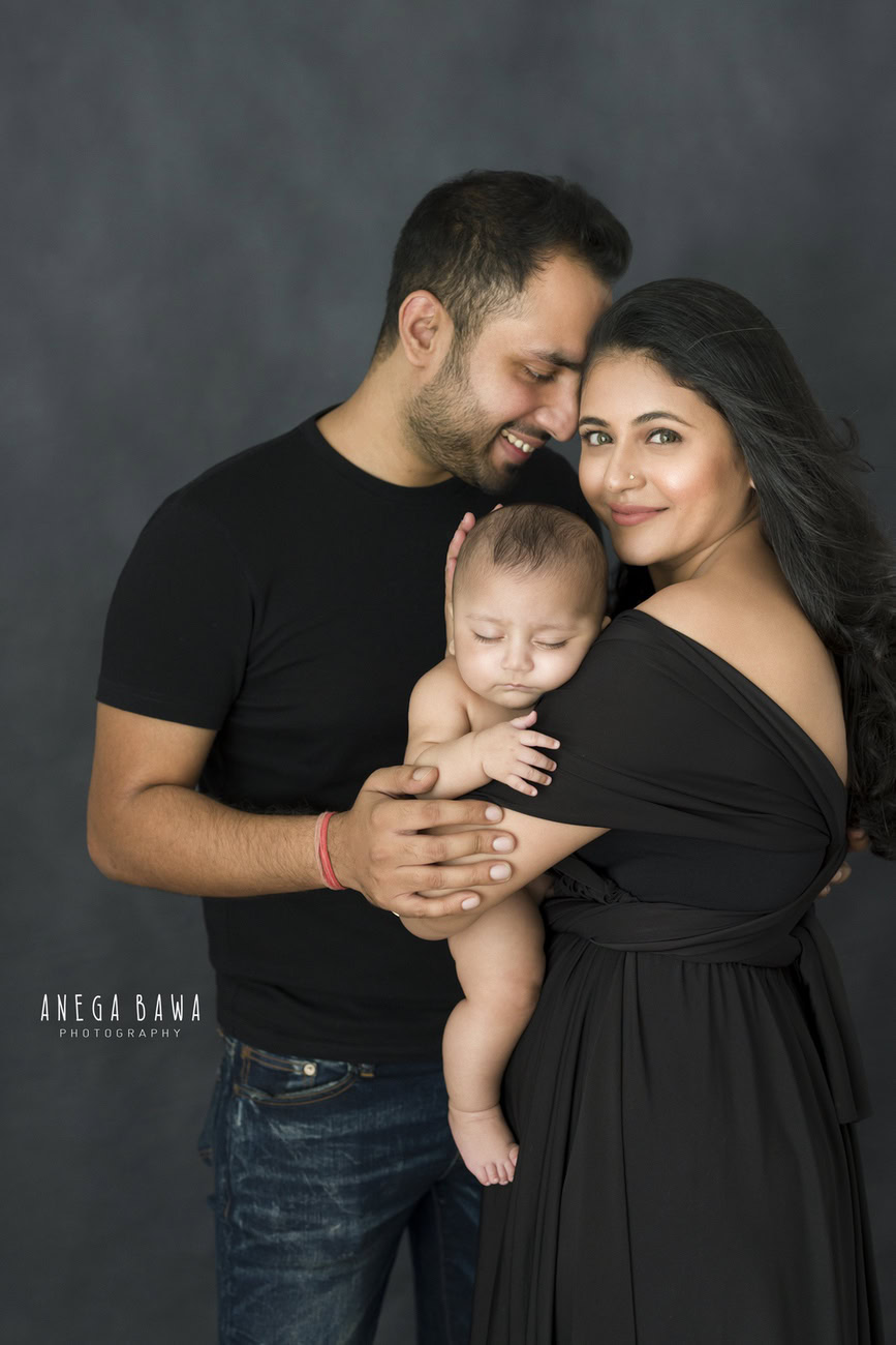 Captivating family photoshoot by Anega Bawa Photography, the esteemed photographer in Delhi and Gurgaon, capturing the adorable moments of Mom, Dad, and their charming 3, 4, 5, 6-month-old son in a cute pose against a stylish grey backdrop.