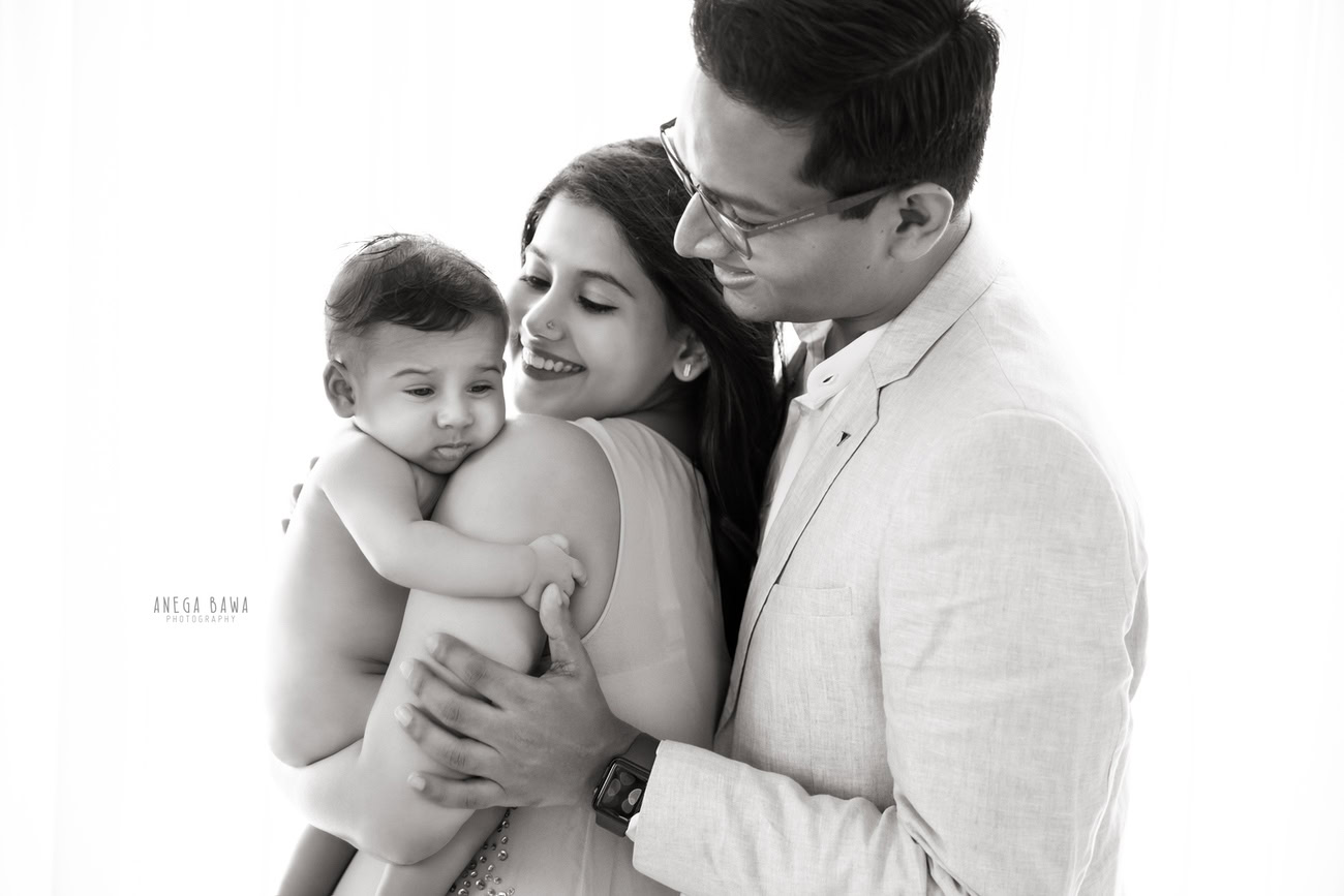 Captivating family photoshoot by Anega Bawa Photography, the esteemed photographer in Delhi and Gurgaon, capturing the endearing moments of Mom, Dad, and their adorable 3, 4, 5, 6-month-old son in a cute pose against a serene white backdrop.