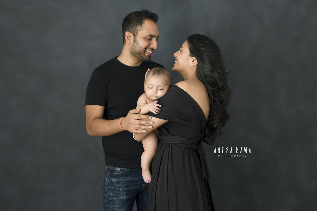 Captivating family photoshoot by Anega Bawa Photography, the esteemed photographer in Delhi and Gurgaon, showcasing the endearing bond of Mom, Dad, and their beloved 3, 4, 5, 6-month-old son against a stylish grey backdrop.