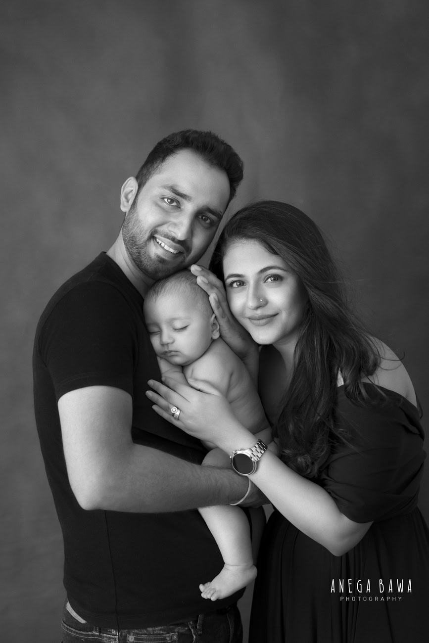 Captivating family photoshoot by Anega Bawa Photography, the esteemed photographer in Delhi and Gurgaon, capturing the heartwarming embrace of Mom, Dad, and their beloved 3, 4, 5, 6-month-old son in a hugging pose against a stylish grey backdrop.