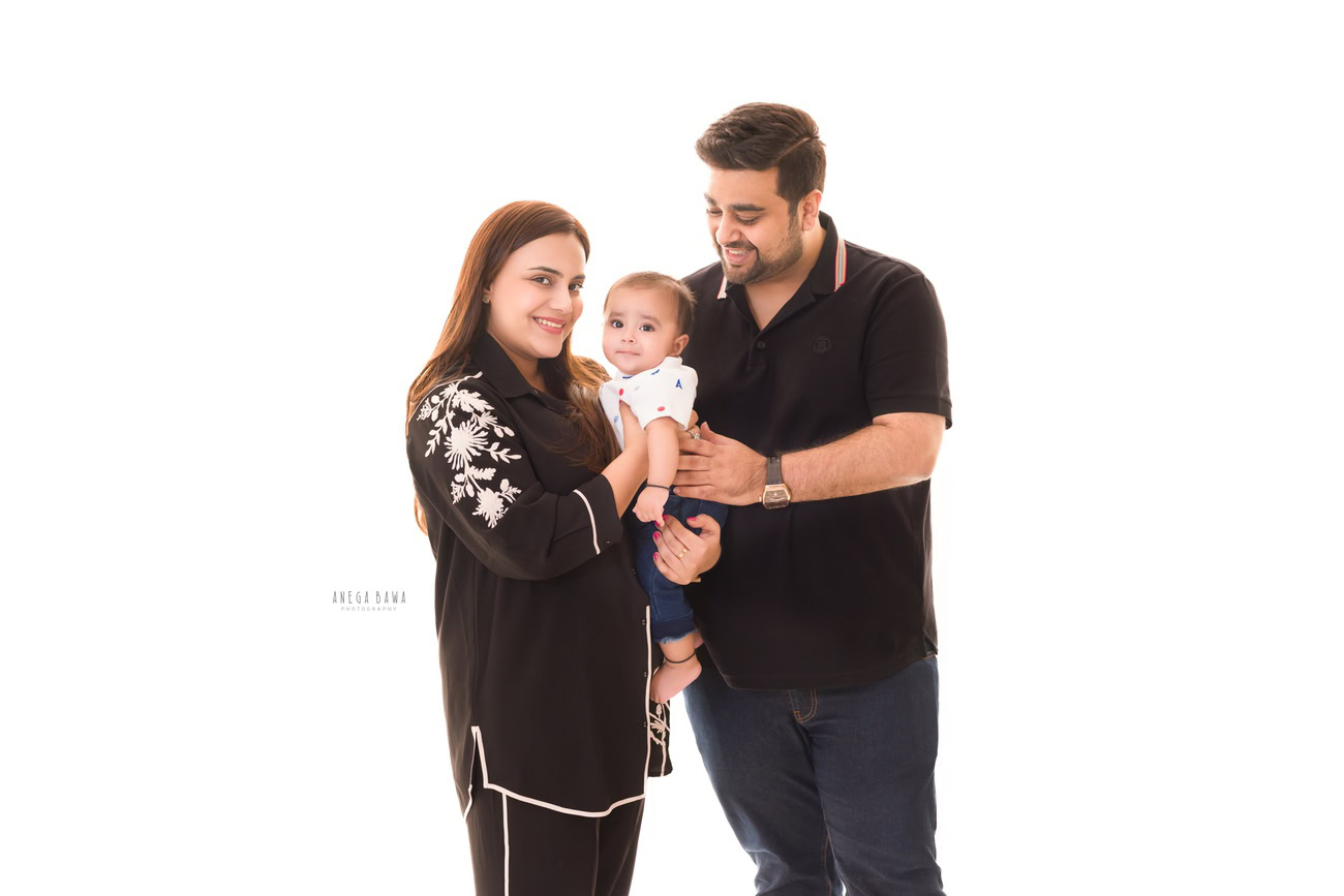Captivating family photoshoot by Anega Bawa Photography, the esteemed photographer in Delhi and Gurgaon, capturing the precious moments of Mom, Dad, and their adorable 3, 4, 5, 6-month-old son posing cutely against a timeless white backdrop.