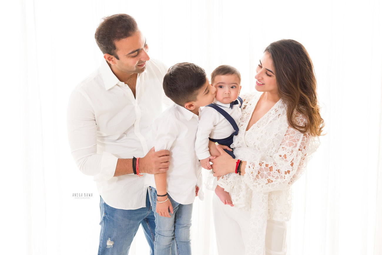 Captivating family photoshoot by Anega Bawa Photography, the esteemed photographer in Delhi and Gurgaon, featuring the endearing moments of Mom, Dad, and their precious 3, 4, 5, 6-month-old son and sibling, all dressed in white attire, against a pristine white backdrop.