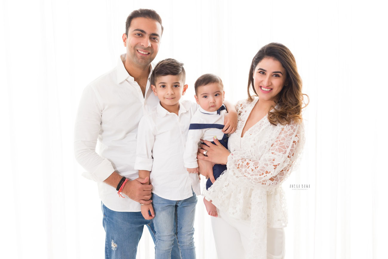 Captivating family photoshoot by Anega Bawa Photography, the esteemed photographer in Delhi and Gurgaon, featuring the endearing moments of Mom, Dad, and their precious 3, 4, 5, 6-month-old son and sibling, all dressed in white attire, against a pristine white backdrop.