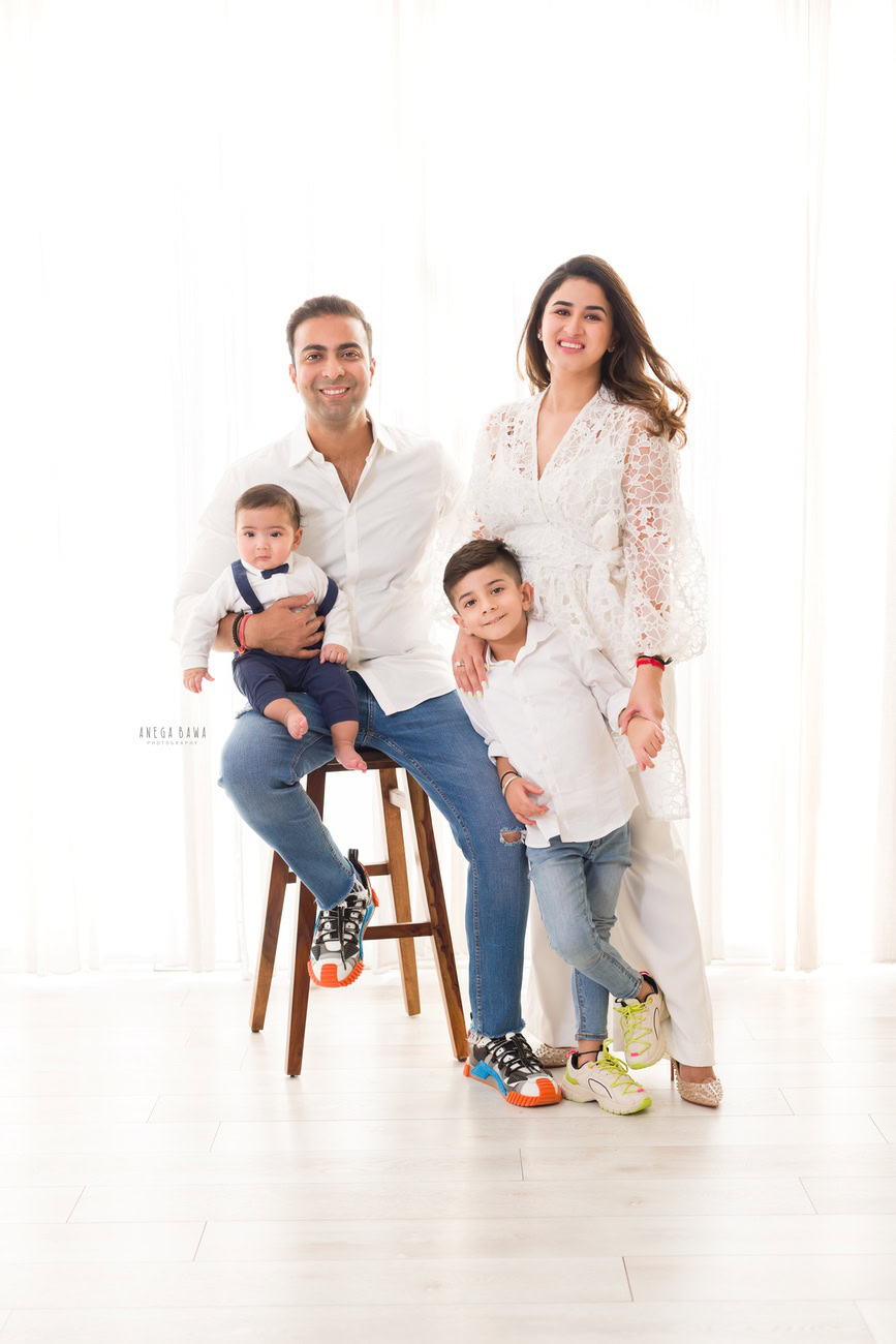 Captivating family photoshoot by Anega Bawa Photography, the esteemed photographer in Delhi and Gurgaon, featuring the endearing moments of Mom, Dad, and their precious 3, 4, 5, 6-month-old son and sibling, all dressed in white attire, against a pristine white backdrop.