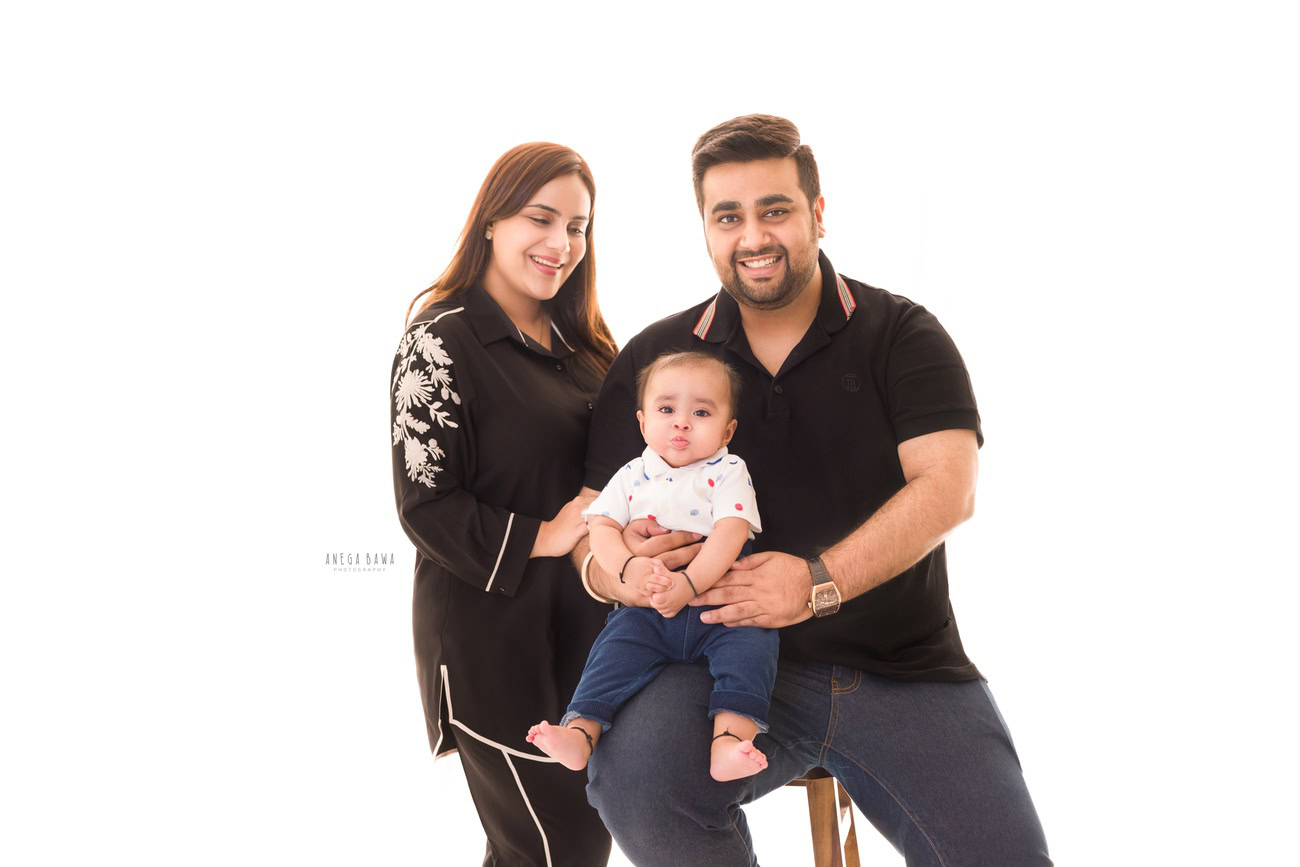 Captivating family photoshoot by Anega Bawa Photography, the esteemed photographer in Delhi and Gurgaon, featuring the lovely moments shared by Mom, Dad, and their adorable 3, 4, 5, 6-month-old son, all dressed in white, against a pristine white backdrop.
