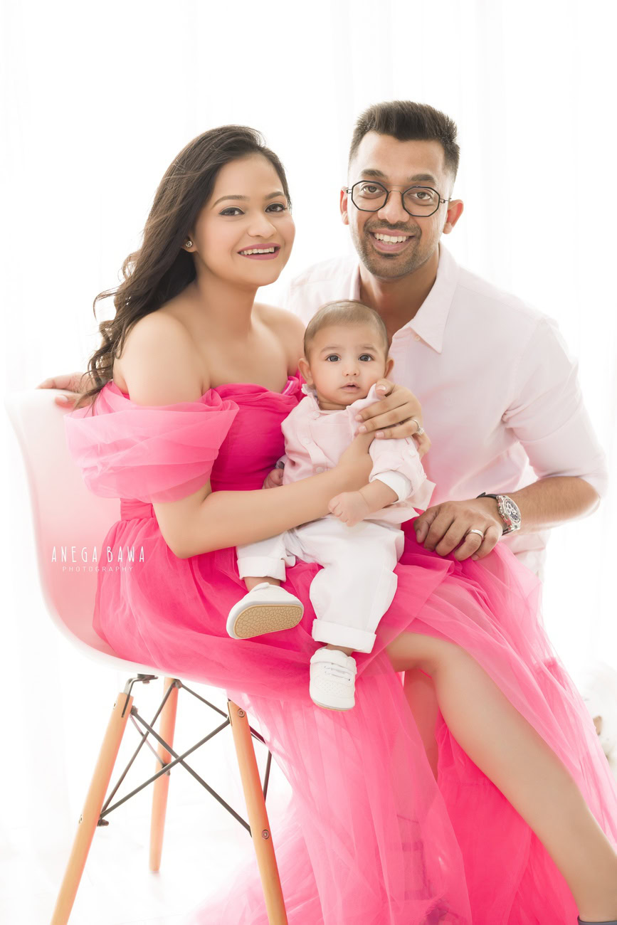Captivating family photoshoot by Anega Bawa Photography, the esteemed photographer in Delhi and Gurgaon, featuring Mom, Dad, and their precious 3, 4, 5, 6-month-old son sitting on Mom's lap, against a serene white backdrop.
