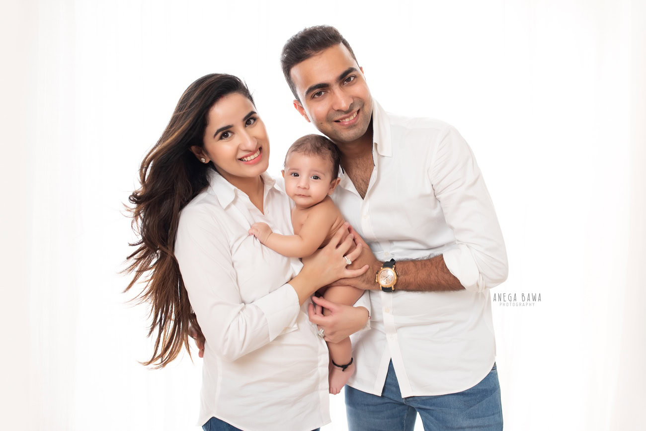 Captivating family photoshoot by Anega Bawa Photography, the esteemed photographer in Delhi and Gurgaon, featuring the cherished moments of Mom, Dad, and their adorable 3, 4, 5, 6-month-old son against a timeless white backdrop.