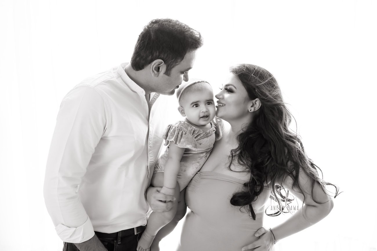 Captivating family photoshoot by Anega Bawa Photography, the esteemed photographer in Delhi and Gurgaon, featuring the endearing moments shared by Mom, Dad, and their precious 3, 4, 5, 6-month-old daughter against a timeless white backdrop.