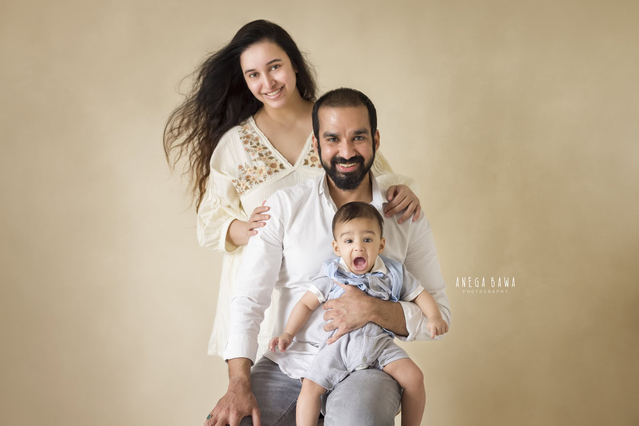 Captivating family photoshoot by Anega Bawa Photography, the esteemed photographer in Delhi and Gurgaon, capturing the joyous moments of Mom and Dad smiling with their precious 3, 4, 5, 6-month-old baby against a warm beige backdrop.