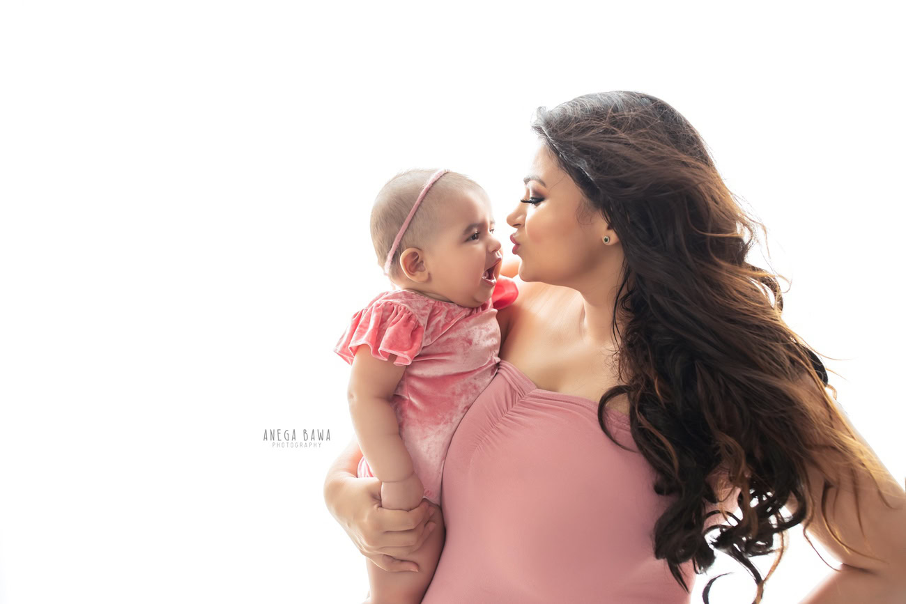 Captivating family photoshoot by Anega Bawa Photography, celebrated in Delhi and Gurgaon, capturing the tender bond between Mom and daughter in a sweet kissing pose against a pristine white backdrop.