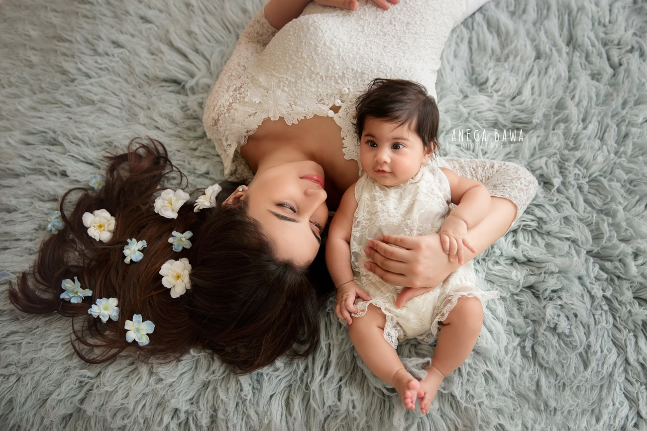 Captivating family photoshoot by Anega Bawa Photography, renowned in Delhi and Gurgaon, showcasing the serene bond between Mom and daughter in a tranquil lying pose on a grey rug against a sophisticated grey backdrop.