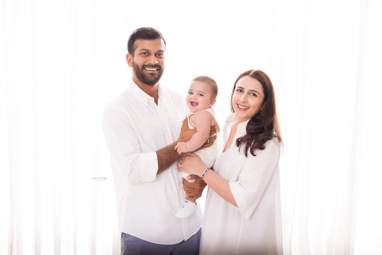 Captivating family photoshoot by Anega Bawa Photography, celebrated in Delhi and Gurgaon, featuring a heartwarming smiling pose of Mom, girl, and Dad against a serene white backdrop.