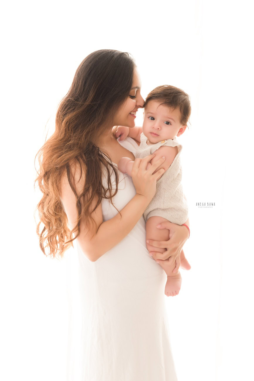 Captivating family photoshoot by Anega Bawa Photography, esteemed in Delhi and Gurgaon, showcasing the endearing moment of Mom kissing her son against a pristine white backdrop.