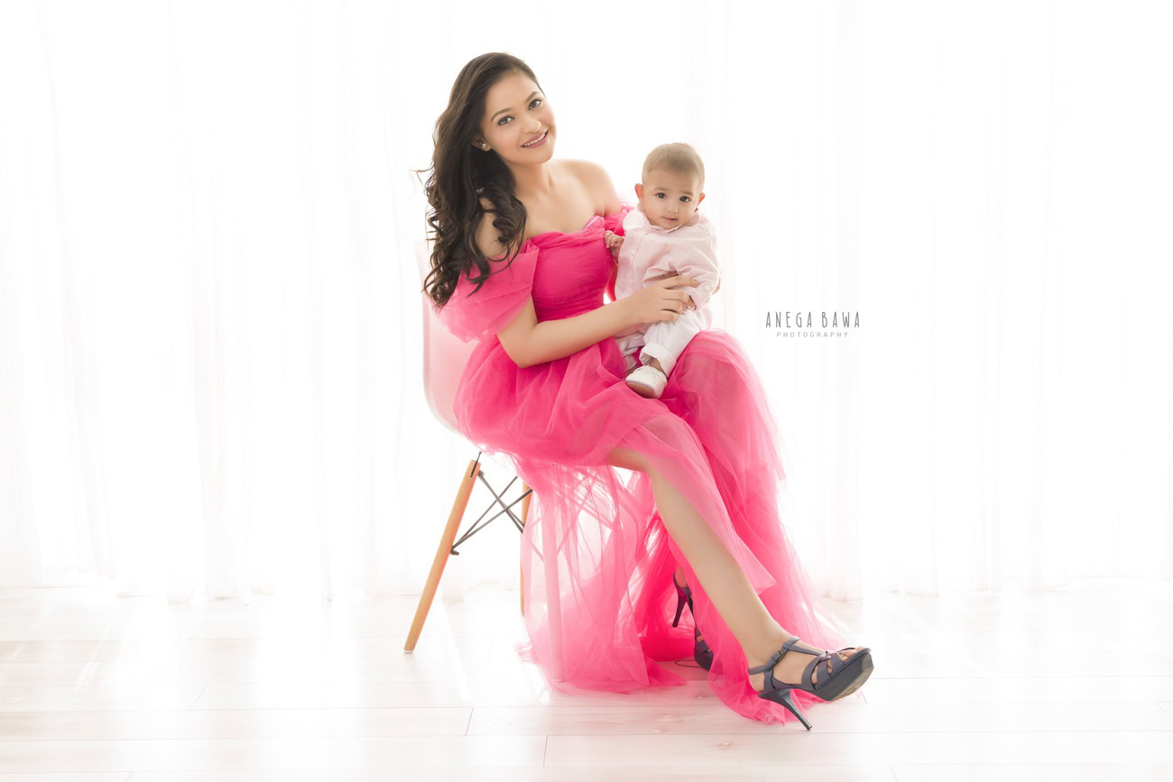 Captivating family photoshoot by Anega Bawa Photography, cherished in Delhi and Gurgaon, showcasing Mom in a pink dress and her son posing charmingly against a pristine white backdrop.