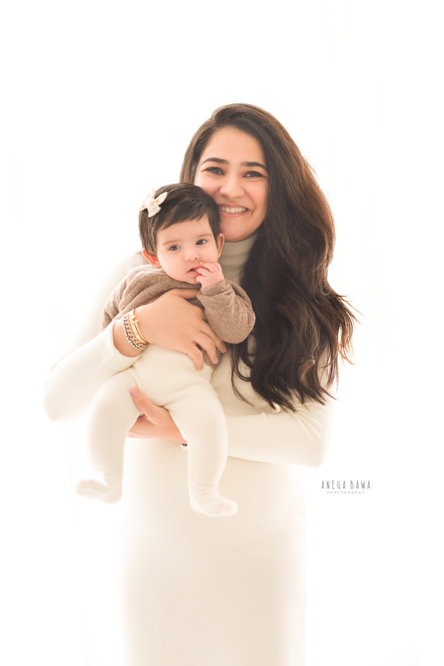 Captivating family photoshoot by Anega Bawa Photography, renowned in Delhi and Gurgaon, capturing Mom posing with her daughter, adorned with a cute headband, against a pristine white backdrop.