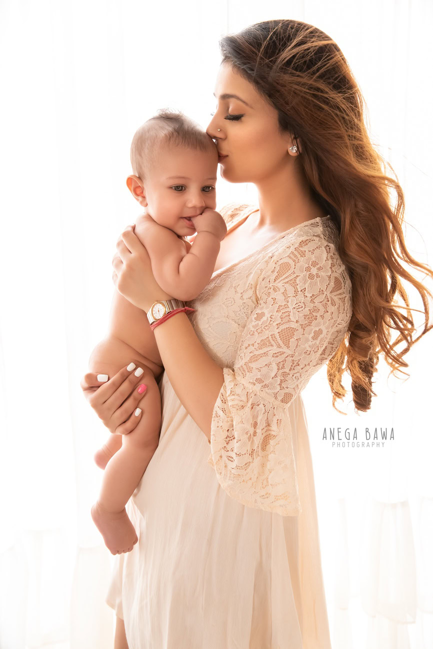 Captivating family photoshoot by Anega Bawa Photography, renowned in Delhi and Gurgaon, capturing a tender moment between Mom and son in a cute kissing pose against a serene white backdrop.