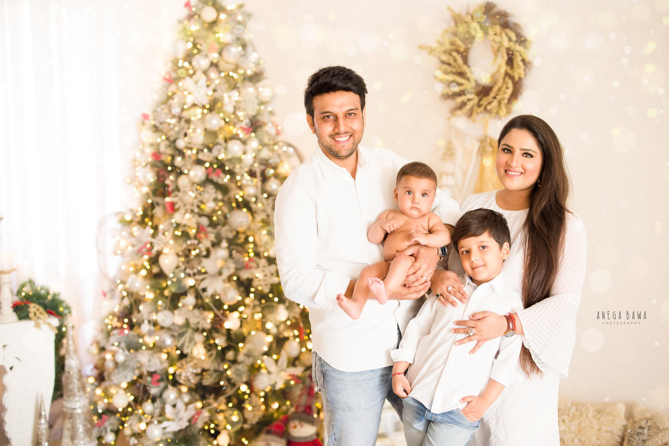 Gather your beautiful family for a memorable photoshoot with Anega Bawa Photography in Delhi and Gurgaon. Mumma, Papa, Son, and Sibling can create heartwarming moments posing together amidst the festive ambiance of a decorated Christmas tree, wrapped gifts, and twinkling fairy lights against a soothing beige backdrop. Let the joy and love shine through in your family portraits captured by Anega Bawa.