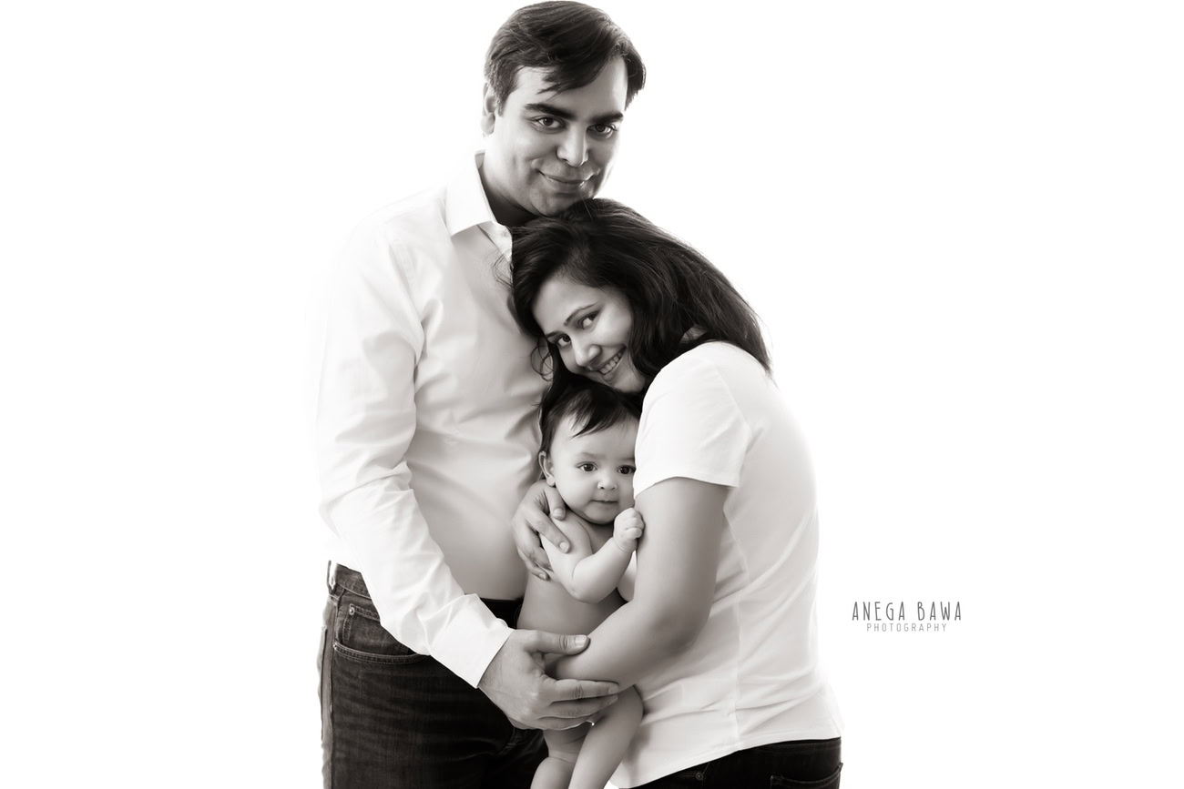Capture the warmth and affection of your family with Anega Bawa Photography in Delhi and Gurgaon. Cherish those heartwarming moments as you and your partner embrace your adorable daughter in a sweet hugging pose against a beautiful white backdrop. Let every smile and cuddle be immortalized in timeless photographs to treasure for years to come.