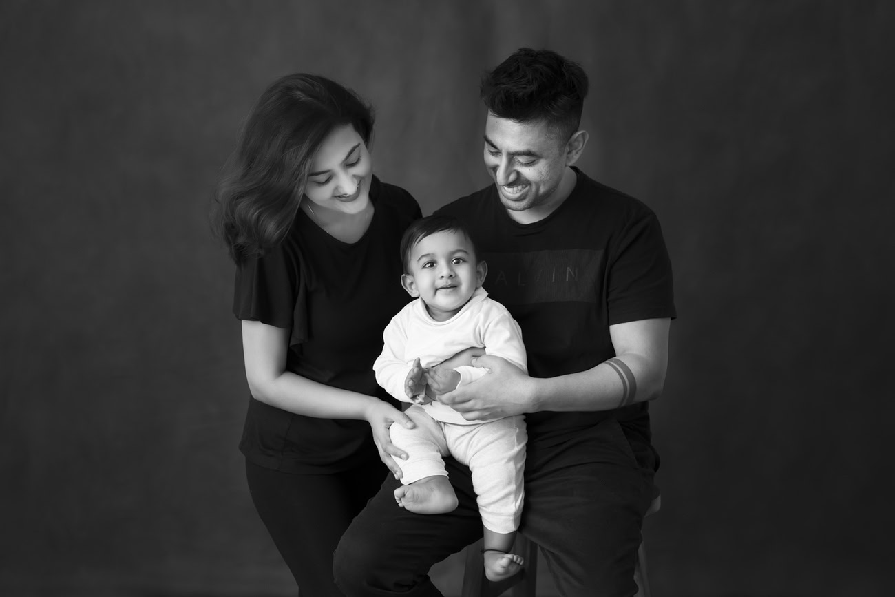 Capture the joyous moments of your family with Anega Bawa Photography in Delhi and Gurgaon. Let your little one shine as they pose with mom and dad against a classic black-and-white backdrop, freezing these precious memories in time with heartwarming smiles.