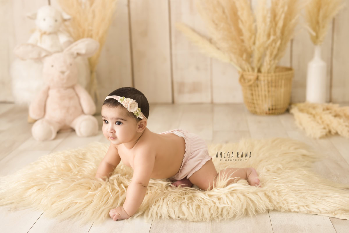 In this adorable toddler photoshoot by Anega Bawa in Delhi, Gurgaon, and Noida, a delightful 12-month-old girl explores the world around her with curiosity and charm. Crawling on a soft beige rug against a soothing beige backdrop, she wears a cute headband that adds to her irresistible charm. Each moment captured in this photoshoot is a testament to her playful spirit and the joy she brings to those around her. These precious memories will be treasured by her family for years to come.