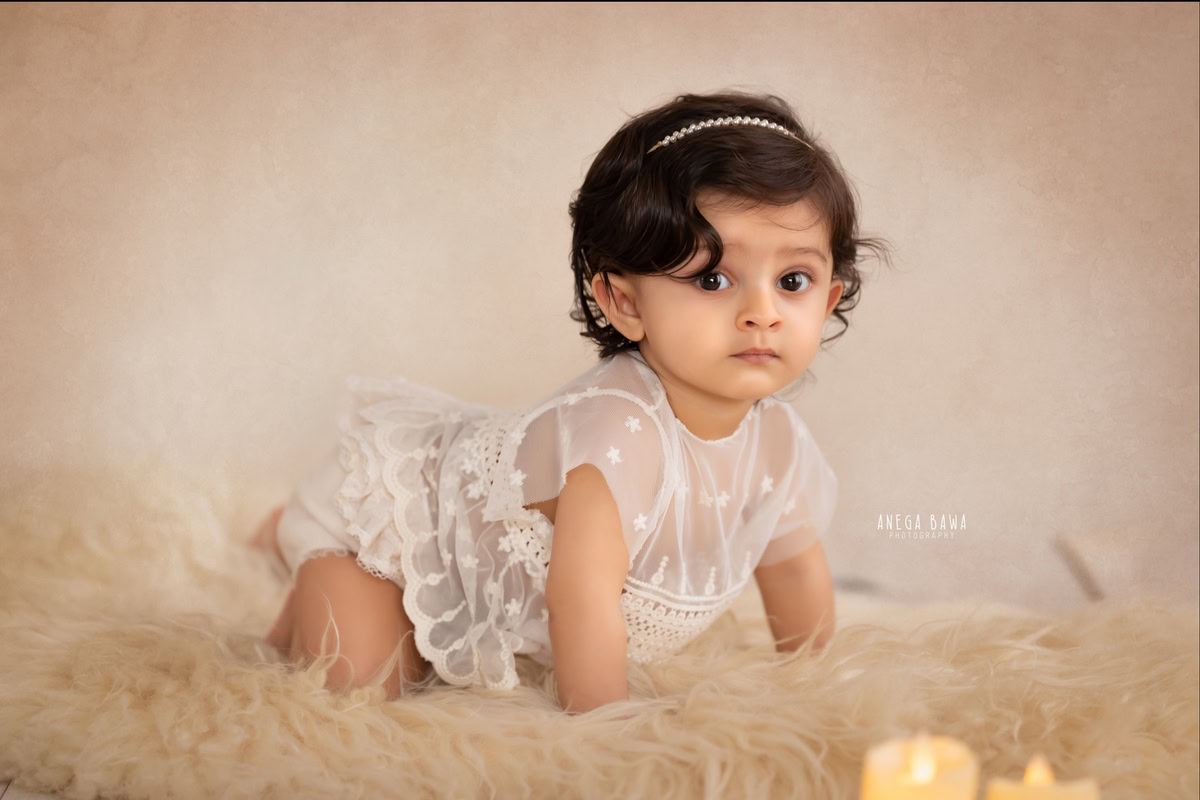 Immerse yourself in the precious moments of your little princess's journey with Anega Bawa Photography in Delhi and Gurgaon. Watch as she crawls gracefully on a soft beige rug, surrounded by warm candlelight against a calming beige backdrop. This enchanting scene captures her innocence and curiosity at 12 months to 1 year old, creating timeless memories to treasure forever.