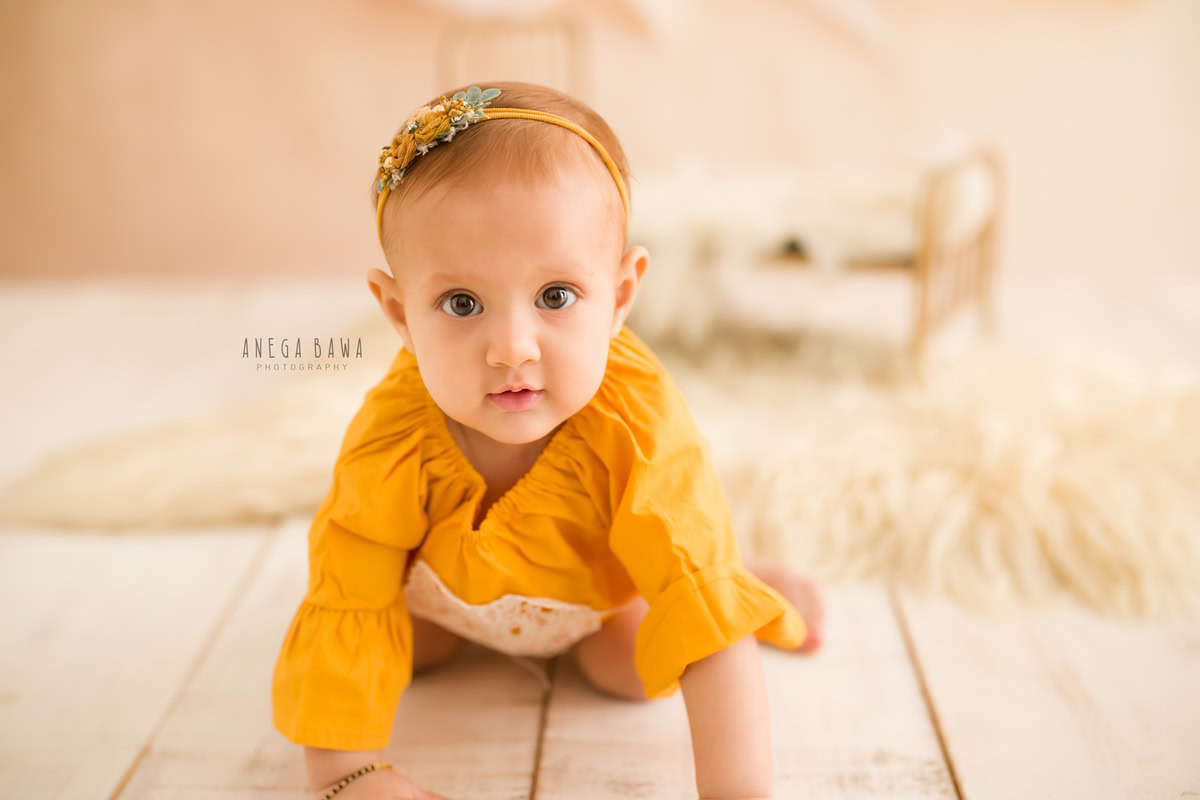 Capture the precious moments of your 12-month to 1-year-old princess with Anega Bawa Photography in Delhi and Gurgaon. Watch her explore the world, adorned with a cute headband, against a soothing beige backdrop. Cherish these heartwarming memories forever.