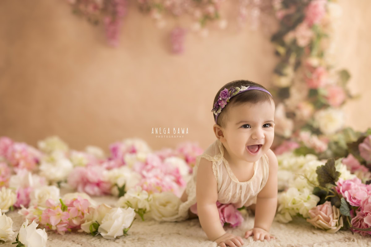 In this enchanting toddler photoshoot by Anega Bawa in Delhi, Gurgaon, and Noida, a sweet 12-month-old girl is captured exploring her world with innocence and charm. Crawling amidst a bed of pink and white flowers against a backdrop of soft peach, she wears a cute headband that adds to her adorable look. Each snapshot captures her curiosity and wonder, making for timeless memories for her family to cherish.