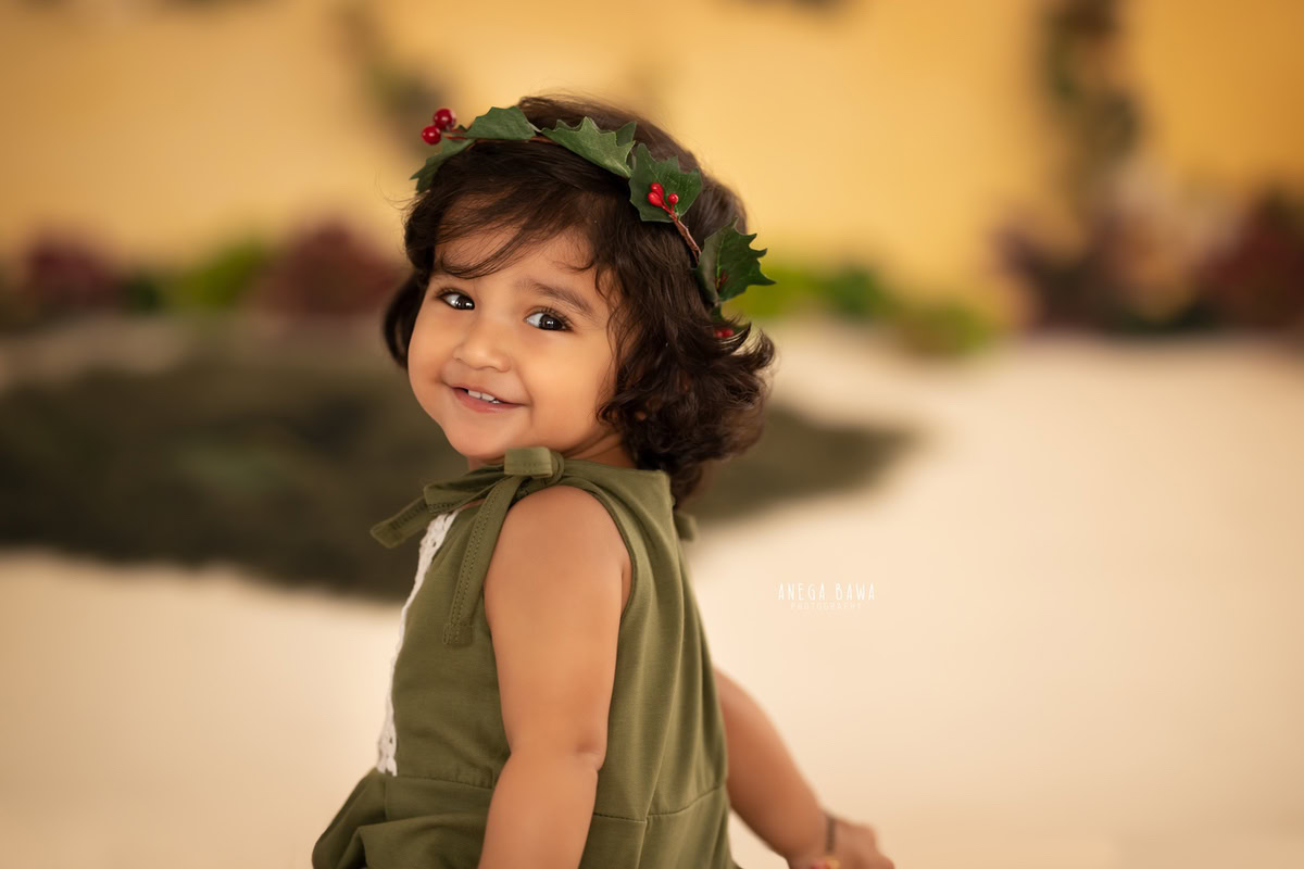 Elevate the beauty of your little princess with Anega Bawa Photography in Delhi and Gurgaon. Watch as she radiates charm with a green tiara band against a vibrant yellow-green backdrop, capturing the essence of her 11-month to 1-year-old innocence in this delightful photoshoot.