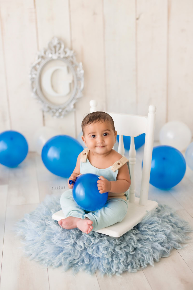 In this enchanting toddler photoshoot by Anega Bawa in Delhi, Gurgaon, and Noida, a delightful 11-month-old girl captivates with her innocence and charm as she holds a vibrant balloon. Against a serene white backdrop complemented by a silver frame on the wall, she adds a touch of magic to the scene. Her playful energy and sweet smile illuminate each frame, creating timeless memories for her family to treasure forever.