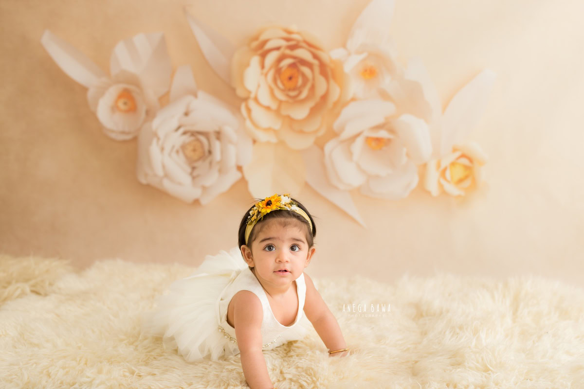 Immerse yourself in the timeless beauty of your little girl with Anega Bawa's sitter photography in Delhi and Gurgaon. Captured at the delicate age of 10 months to 1 year old, she sits gracefully on a beige rug against a peachy floral backdrop. These captivating images will preserve the fleeting moments of her innocence and charm for a lifetime.