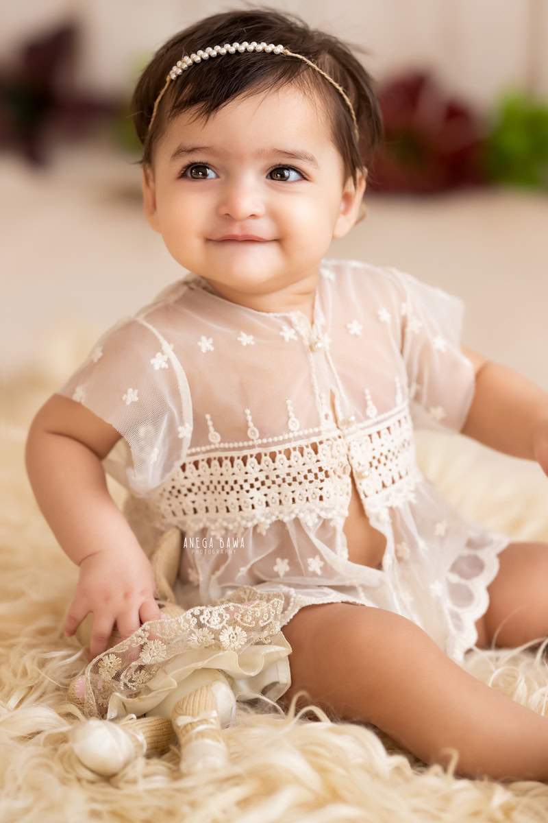 Capture the precious moments of your little princess with Anega Bawa Photography in Delhi and Gurgaon. Dressed in a delicate net dress, she sits gracefully on a beige rug against a soothing beige backdrop, exuding her charming innocence at 10 months to 1 year old.
