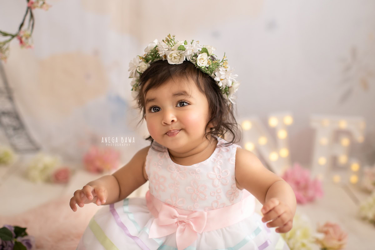 Watch your little princess blossom with joy in a delightful photoshoot by Anega Bawa Photography in Delhi and Gurgaon. Seated amidst a bed of flowers, wearing a charming tiara band, she exudes radiance at 9 months to 1 year old.