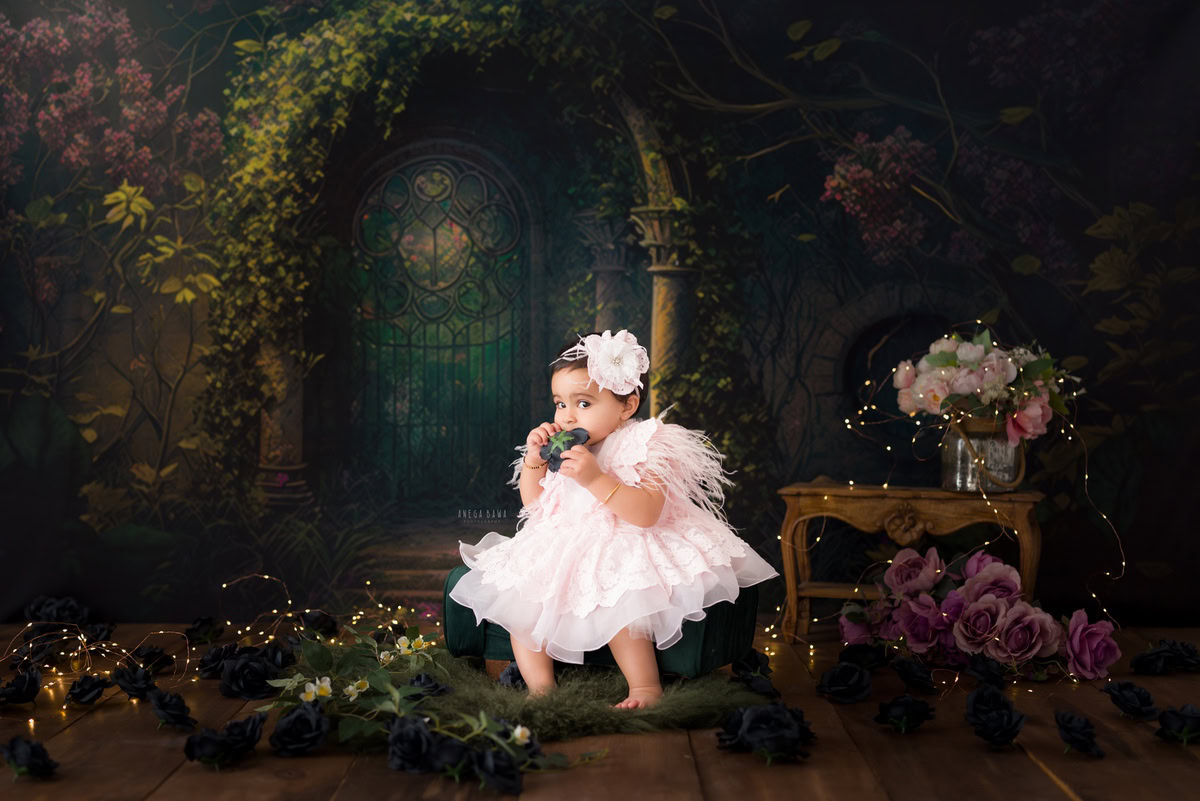 Capture the natural beauty of your little one with Anega Bawa's sitter photography in Delhi and Gurgaon. At 9 months, she sits gracefully, holding a delicate leaf, on a cozy brown rug. Against a backdrop of lush greenery, her innocence shines through, creating timeless memories you'll cherish forever.