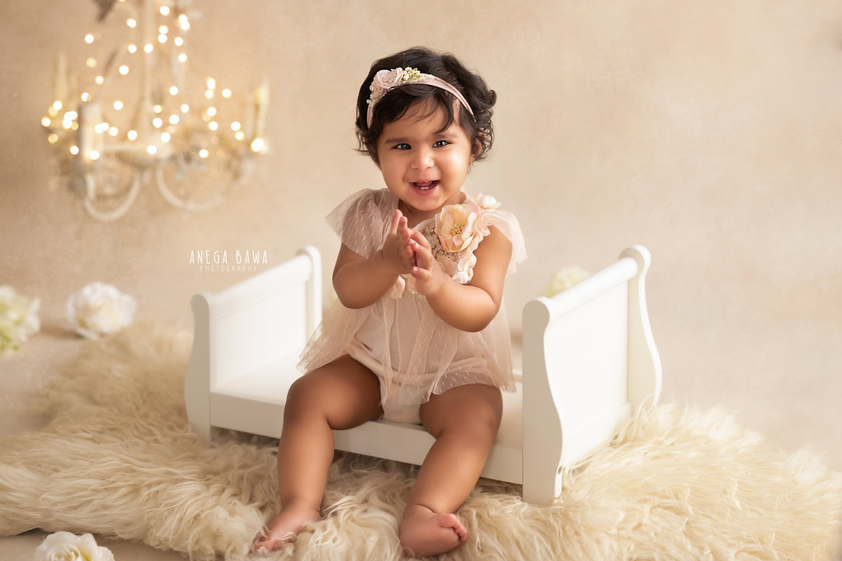 Celebrate the innocence of your little angel with Anega Bawa Photography in Delhi and Gurgaon. Nestled in a golden cot against a gentle beige backdrop adorned with floral frames, she creates captivating memories at 9 months to 1 year old.