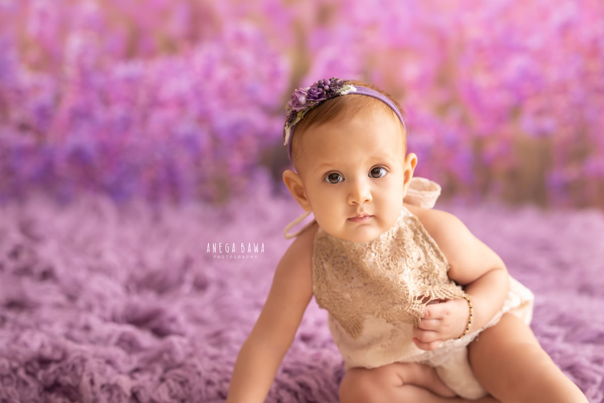 Capture the serene beauty of your little princess with Anega Bawa Photography in Delhi and Gurgaon. Adorned in lavender hues, seated on a lavender rug against a matching backdrop, she exudes tranquility at 8 months to 1 year old, creating timeless memories.