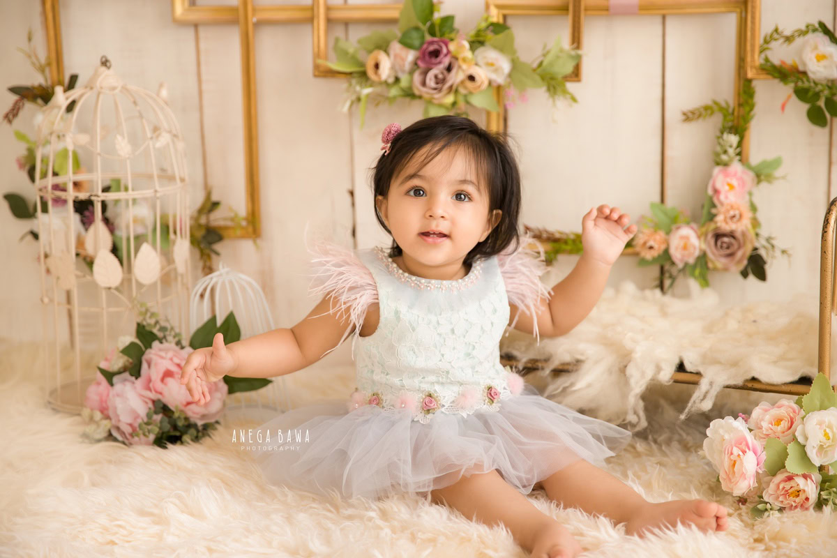 Embark on a journey of enchantment with your little princess through Anega Bawa Photography in Delhi and Gurgaon. Seated on a beige rug amidst pink flowers and castle props, surrounded by floral frames on the wall, she radiates grace at 8 months to 1 year old, weaving a tapestry of timeless memories.
