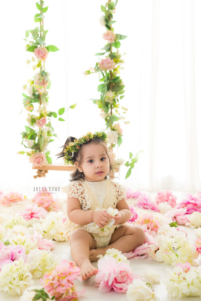 Nestled amidst a carpet of delicate blooms, your little princess sits gracefully, bathed in the soft glow of a serene white backdrop. Each moment captured by Anega Bawa Photography in Delhi and Gurgaon is a timeless testament to the innocence and beauty of your 7-month to 1-year-old.