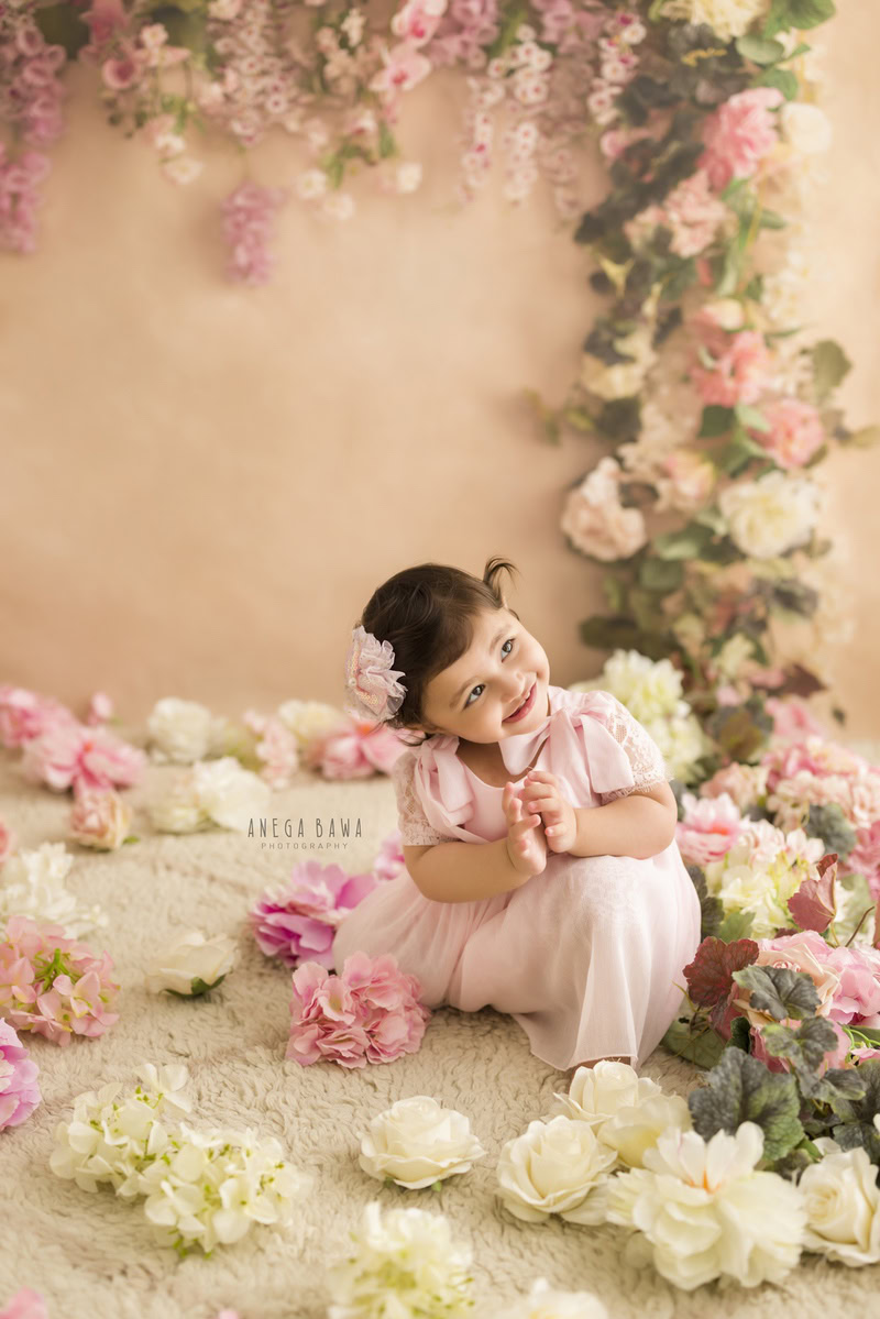 Amidst a gentle palette of peach and white, your little princess sits, adorned with a charming floral accessory in her hair. Against the backdrop of delicate blooms and a serene peach backdrop, Anega Bawa Photography captures the essence of innocence and beauty in your 7-month to 1-year-old.