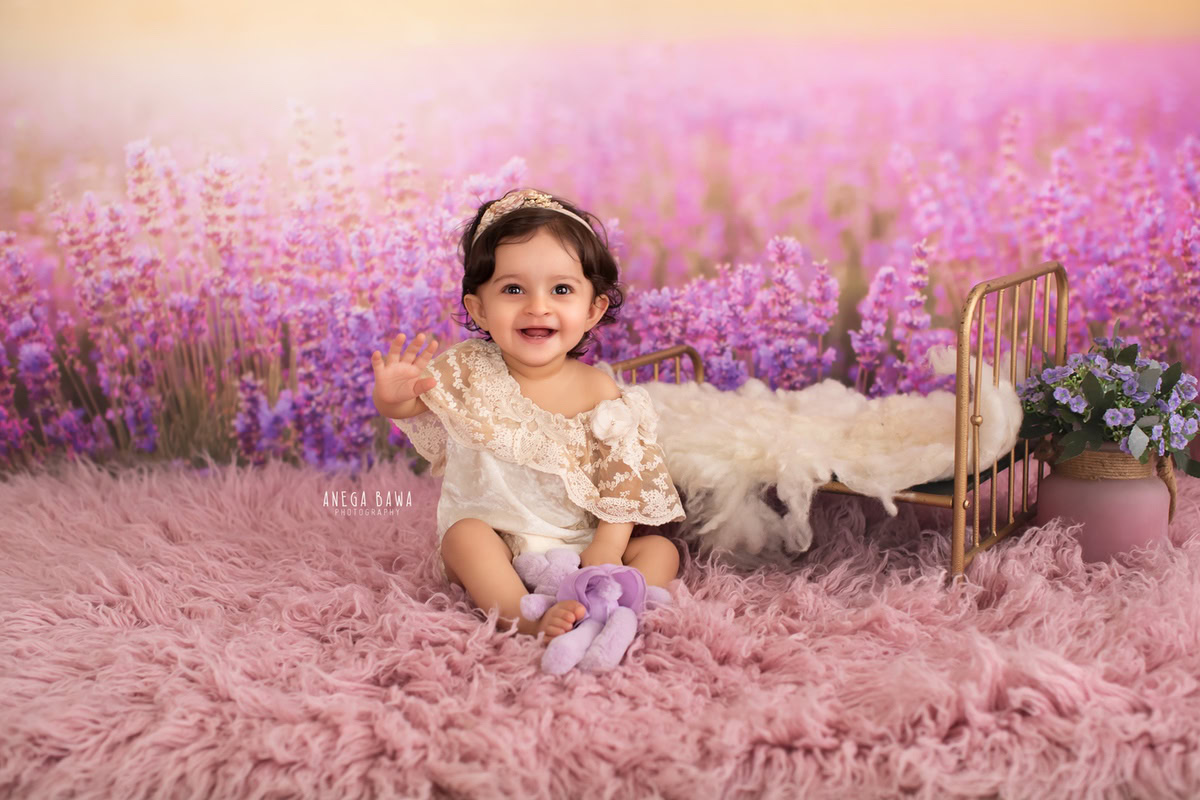 Captured by the talented Anega Bawa in Gurgaon-Delhi, this enchanting photograph portrays a 7-month-old girl seated on a soft pink rug against a backdrop of soothing lavender hues. The golden cot adds a touch of elegance to the scene, creating a captivating ambiance. With expert composition and lighting, the image captures the innocence and charm of infancy, making it a timeless keepsake for the family to cherish for years to come.
